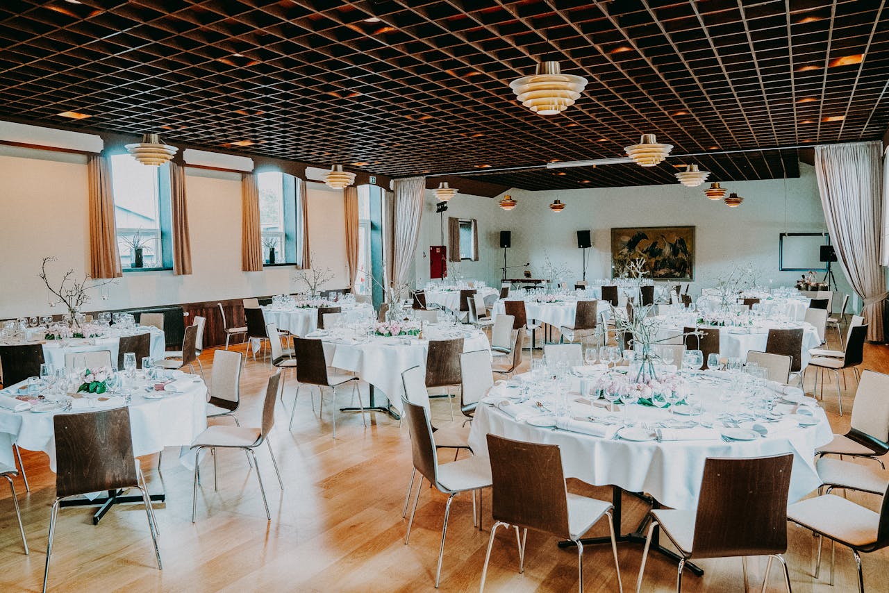 Interior of spacious cozy hall of restaurant with small black chairs around tables decorated with lamps and drapes